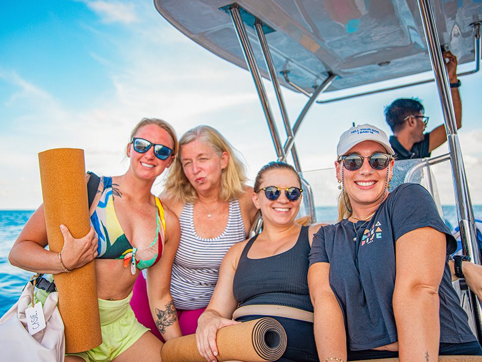 Four smiling women on a boat holding yoga mats
