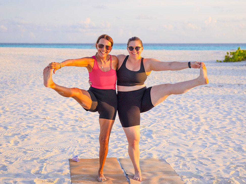 Two women doing the standing hand-to-big-toe pose on beach