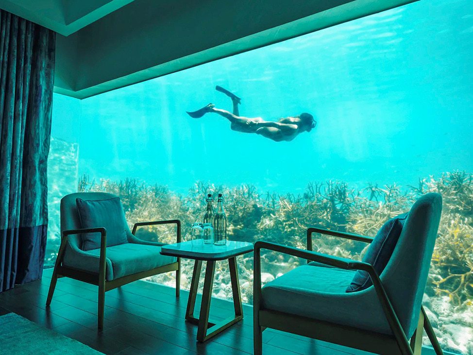 Woman snorkeling in front of window of underwater bungalow in the Maldives